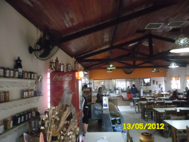Antigo salão do restaurante, doces e bebidas à esquerda, fogão de lenha e cozinha ao fundo